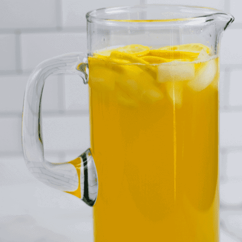 healthy lemonade in a glass pitcher with lemon slices and ice cubes inside.