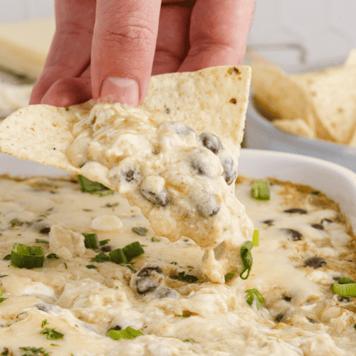 holding a tortilla chip and scooping up the creamy dip.