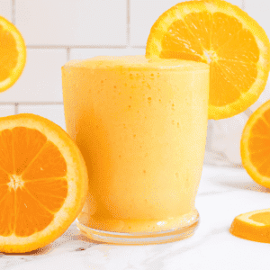 glass of creamy orange mango smoothie with slices of oranges.
