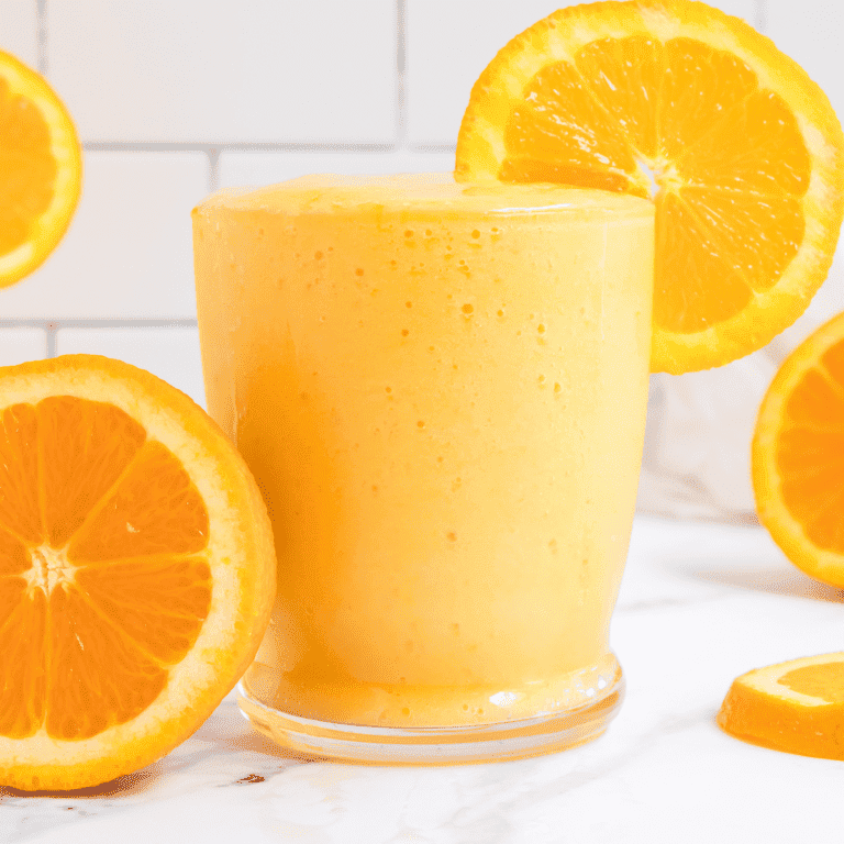glass of creamy orange mango smoothie with slices of oranges.