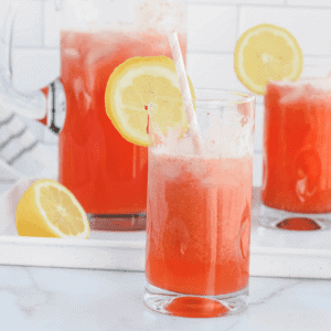 glass pitcher with two large glasses of strawberry lemonade.