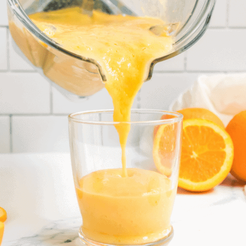 pouring an orange smoothie into a glass from the blender.