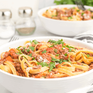 two large white pasta bowls of bolognese sauce over noodles.