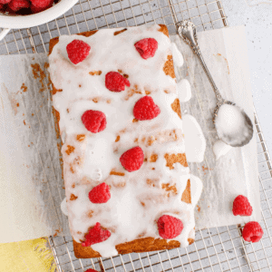 lemon raspberry bread on parchment paper with a spoon for icing.