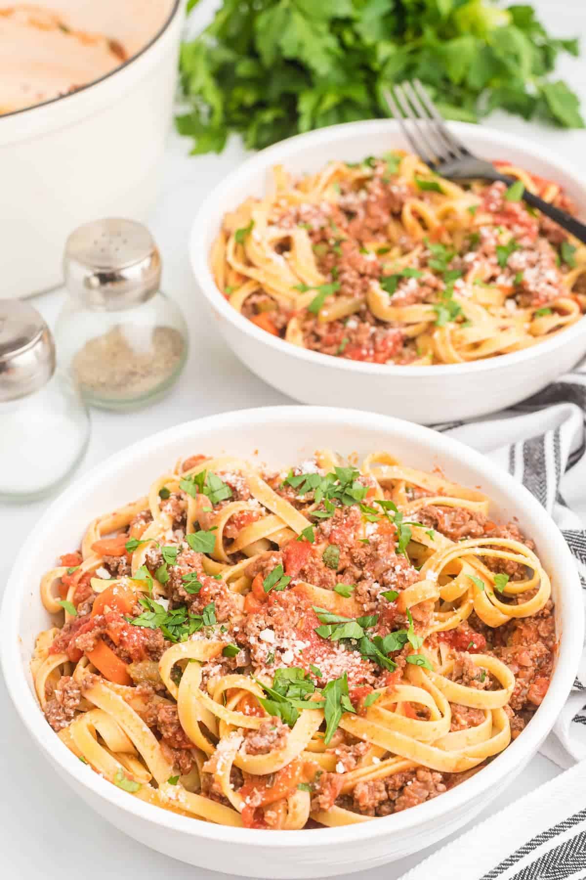 two white bowls filled with the authentic bolognese sauce over pasta noodles.