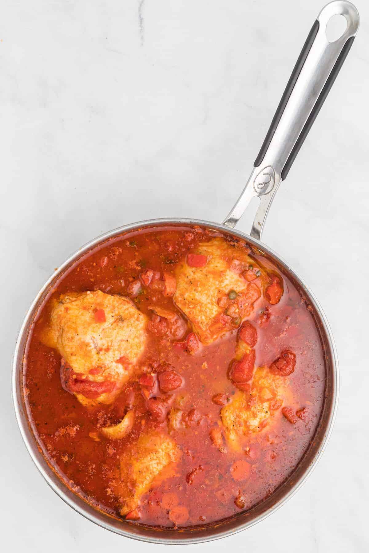 skillet with chicken pieces and tomato sauce.