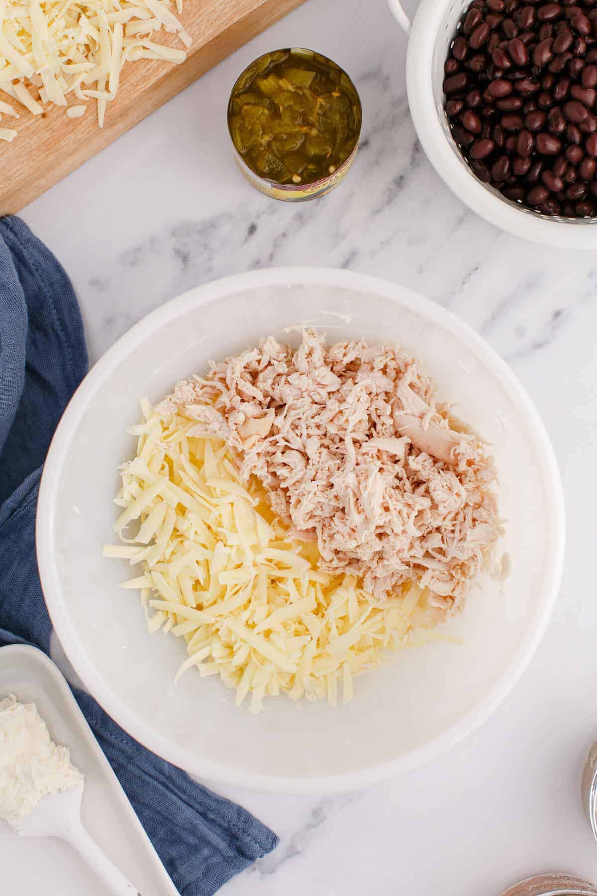 large white bowl with shredded chicken and Monterey cheese.