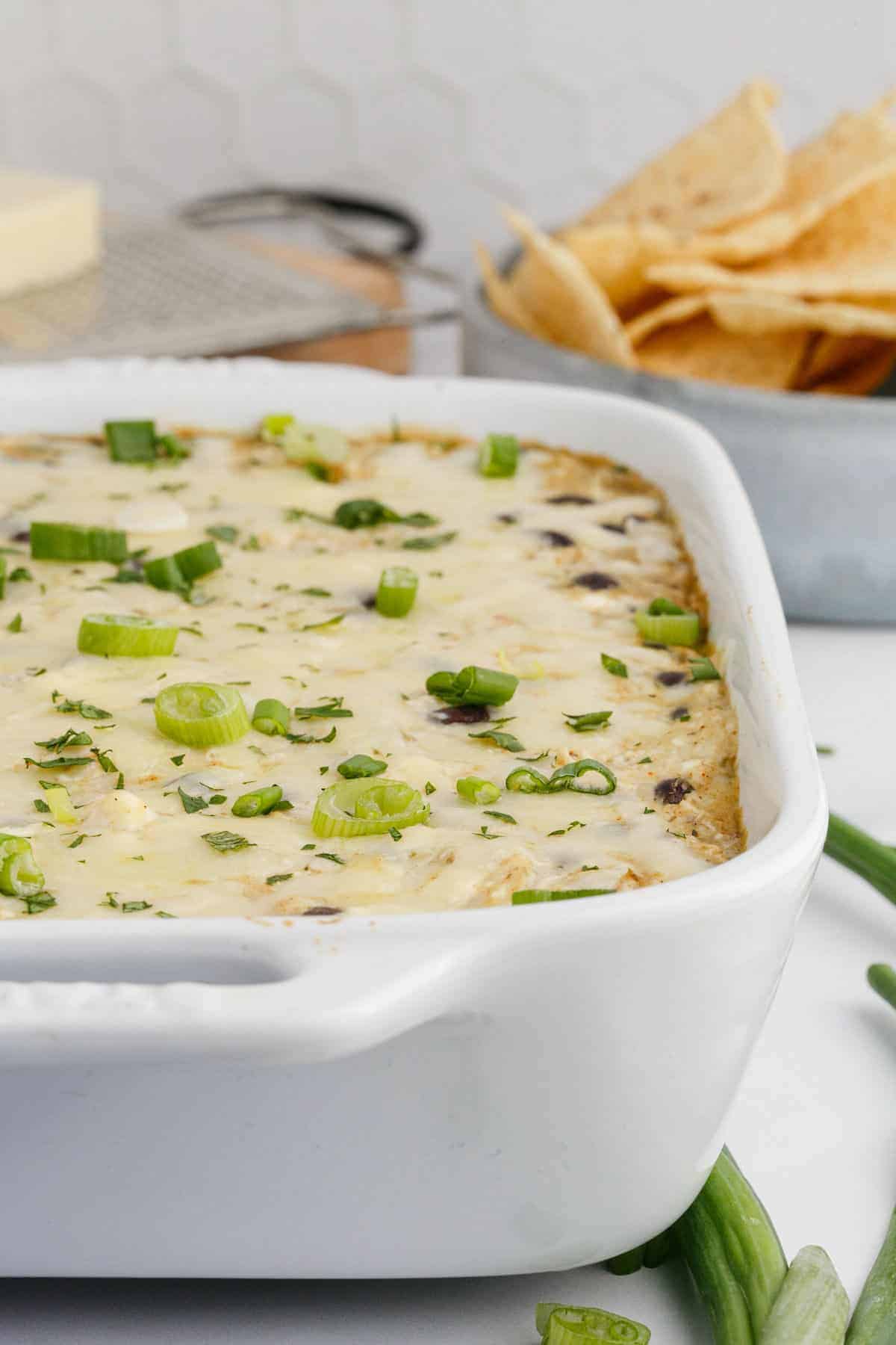 white casserole dish with chicken enchilada dip and a bowl of tortilla chips behind it.