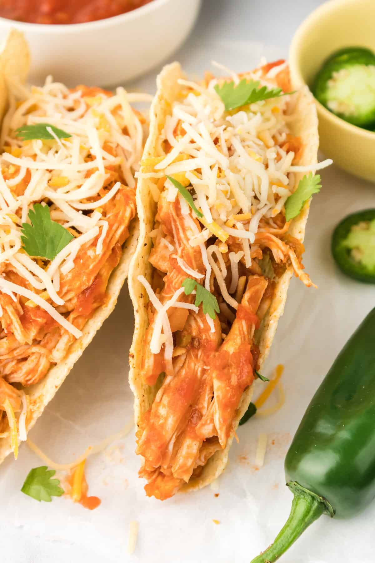 shredded chicken tacos on with counter with jalapenos and salsa in small white bowls. 