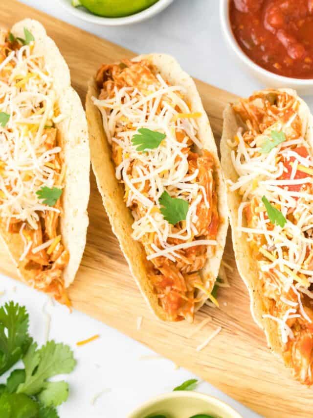 shredded chicken tacos on a wooden board with favorite taco toppings in small white bowls.