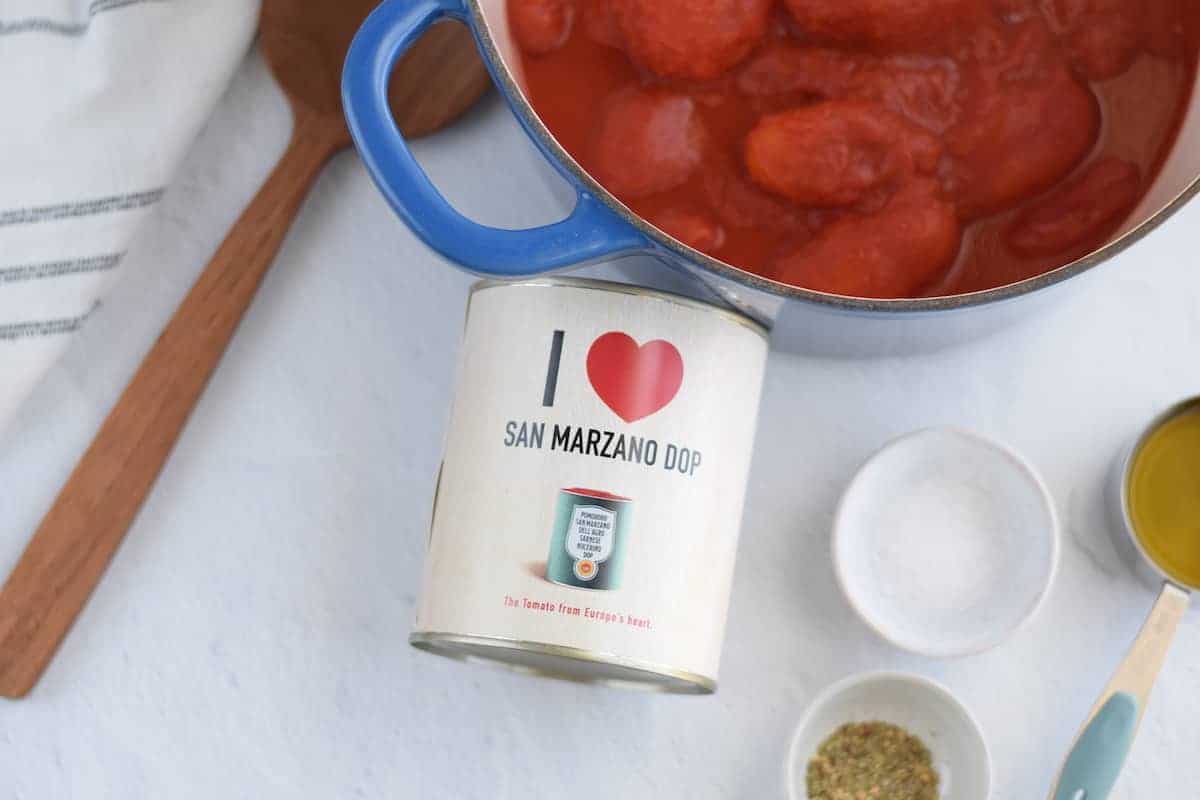 blue dutch oven pot with San Marzano tomatoes and can of tomatoes on the side.