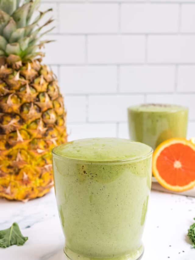 tropical green smoothie in a glass with pineapple in the background.