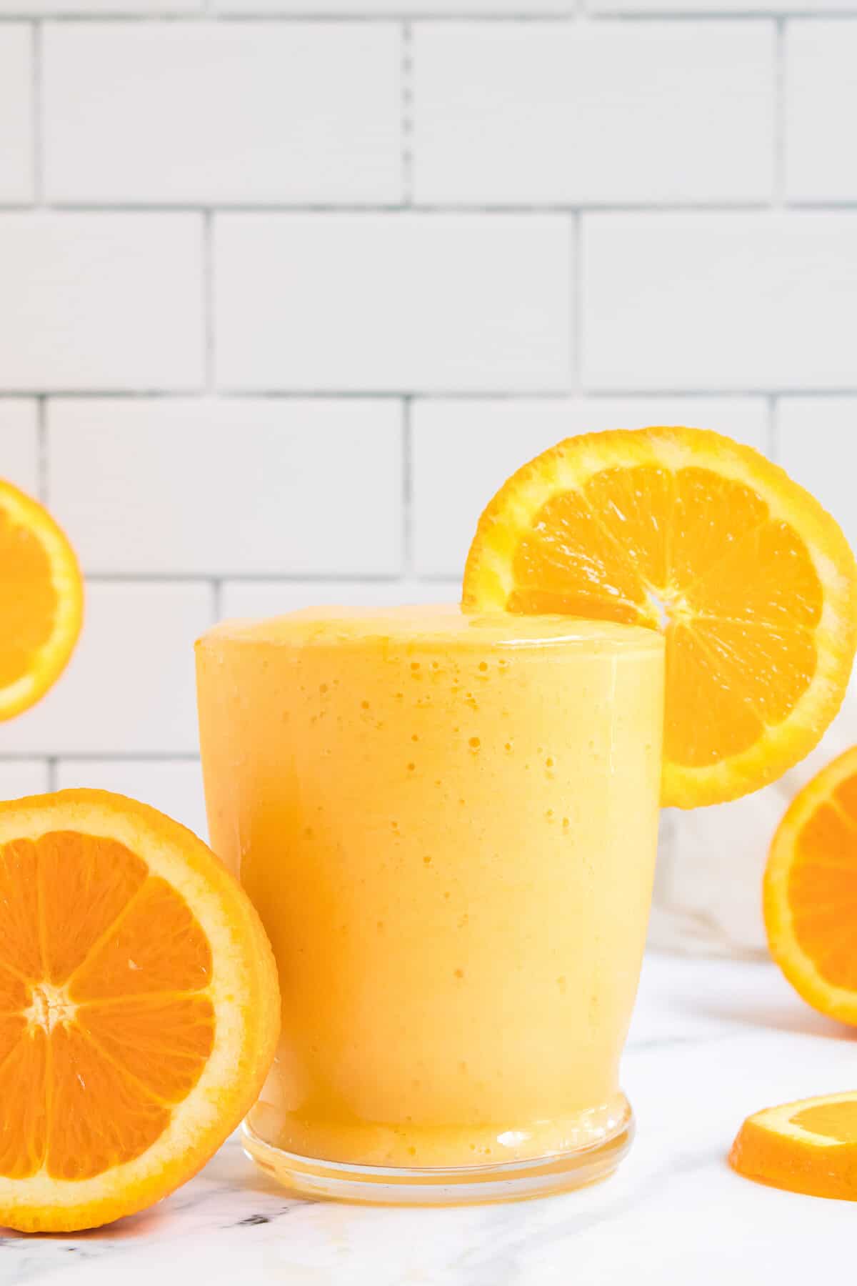 glass filled with mango and orange smoothie with orange wedges.
