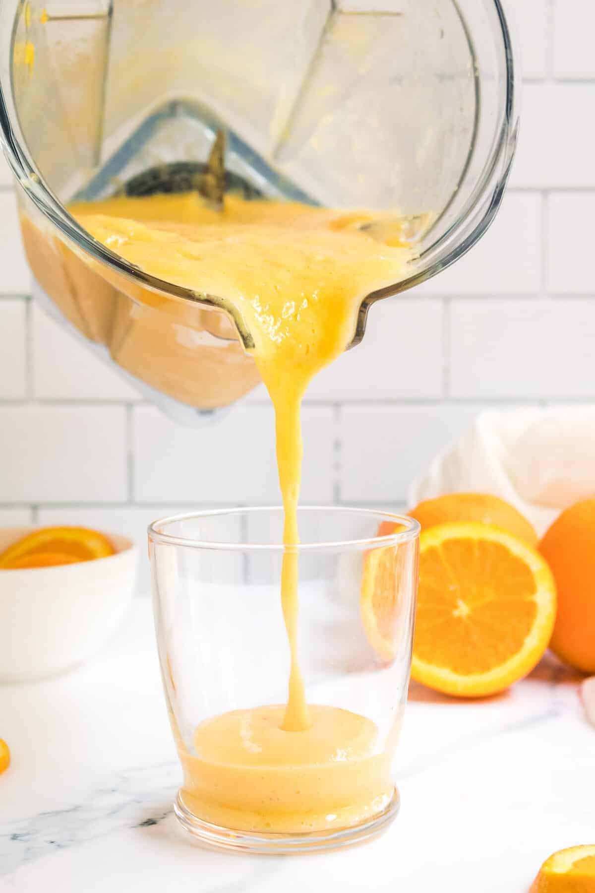 pouring the orange smoothie from the blender into the glass. 