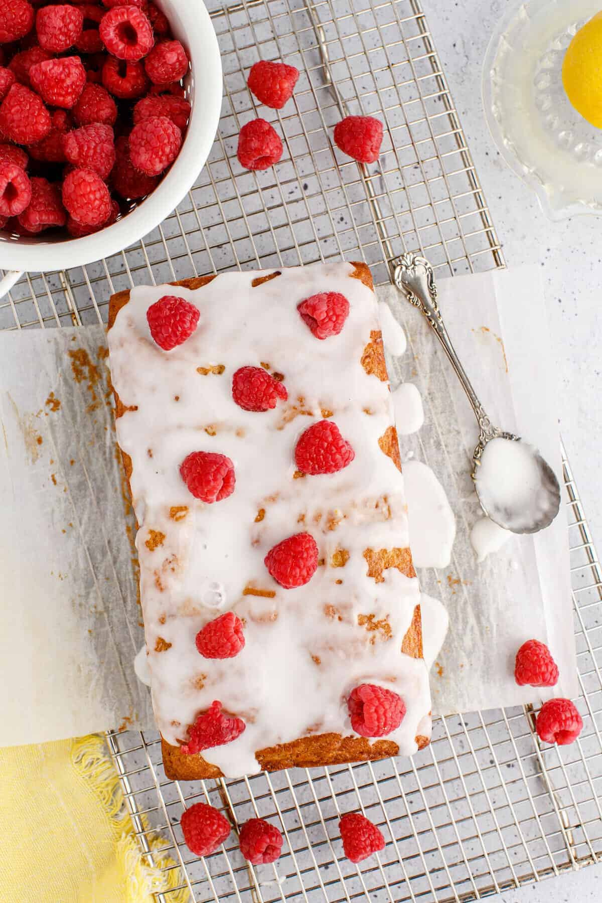 lemon raspberry bread on a parchment paper lined rack with fresh raspberries and glaze.