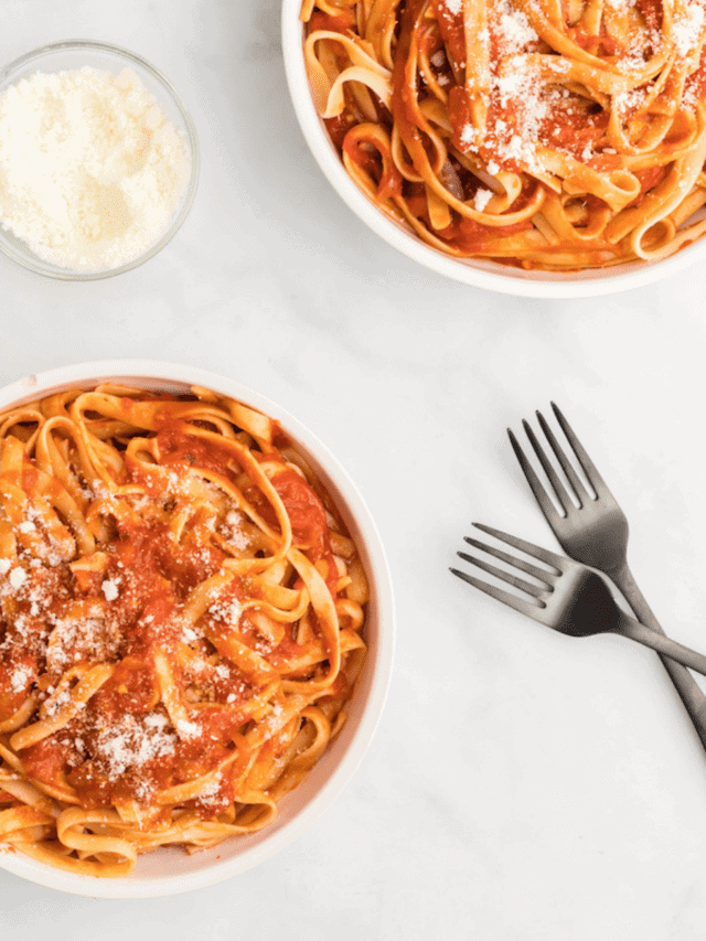 two large white pasta bowls with san Marzano tomato sauce and black forks to the side.