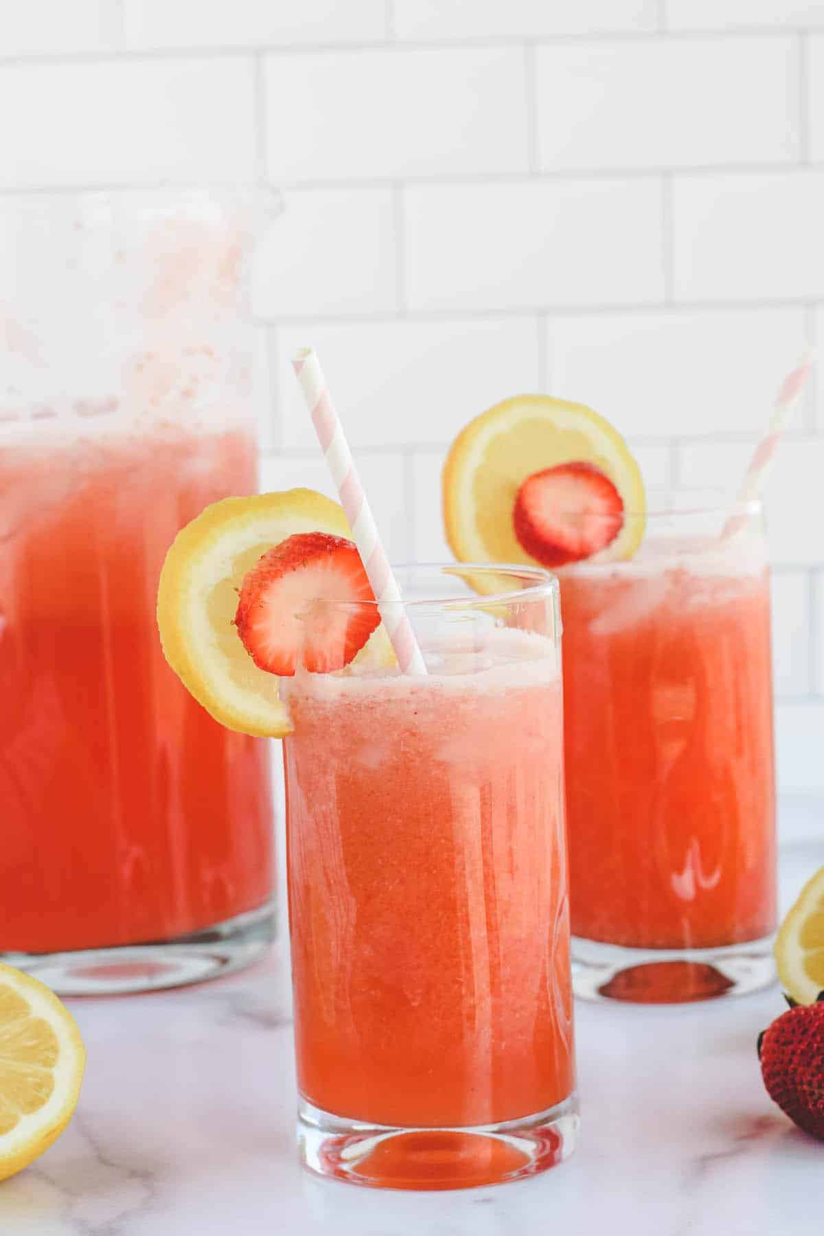 glasses of strawberry lemonade with lemon and strawberry garnishes and paper straws.