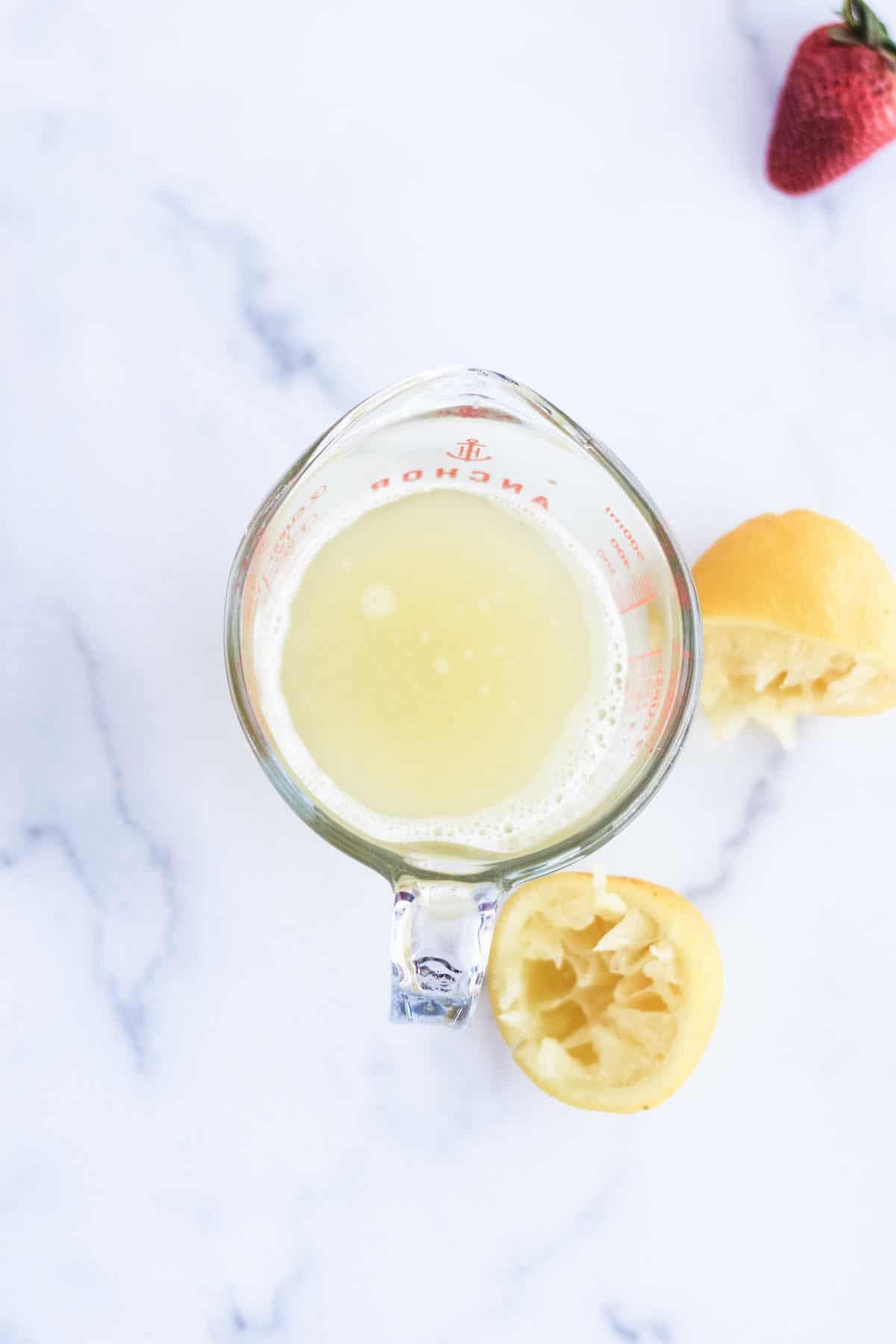 lemon juice in a measuring cup with lemons to the side.