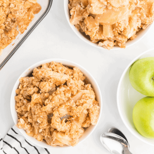 apple crisp in small white bowls with a bowl of green apples to the right of them.
