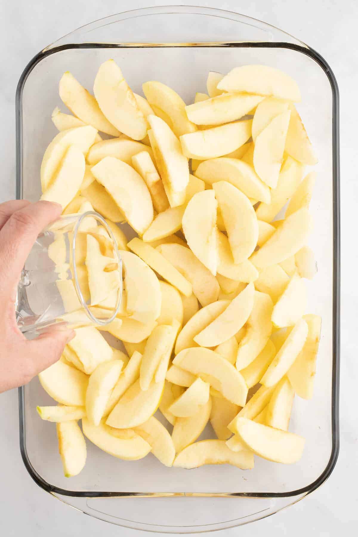 baking dish with apple slices and pouring a little water to the top of the slices.
