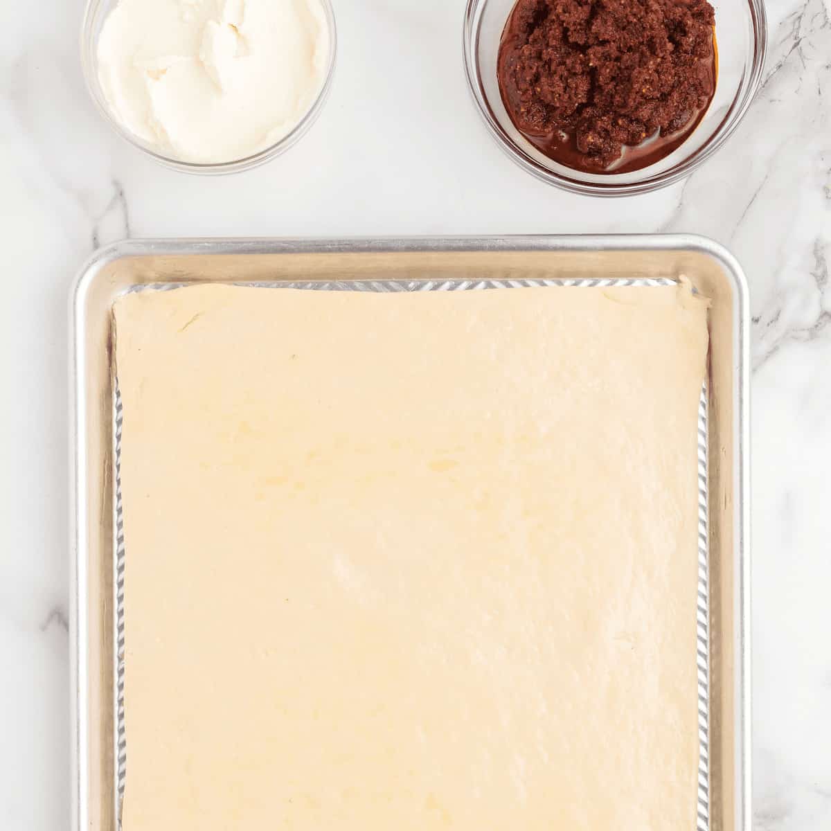 homemade pizza dough rolled out on a rimmed baking sheet.