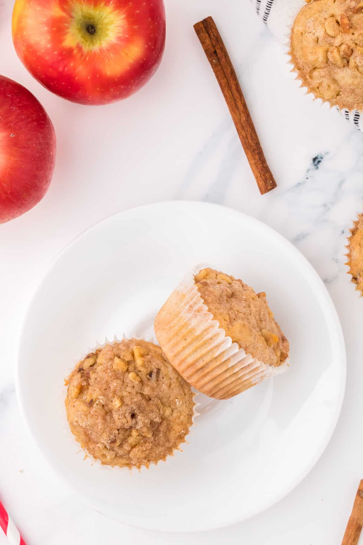 two apple crumb muffins side by side on a white plate with fresh apples in background.