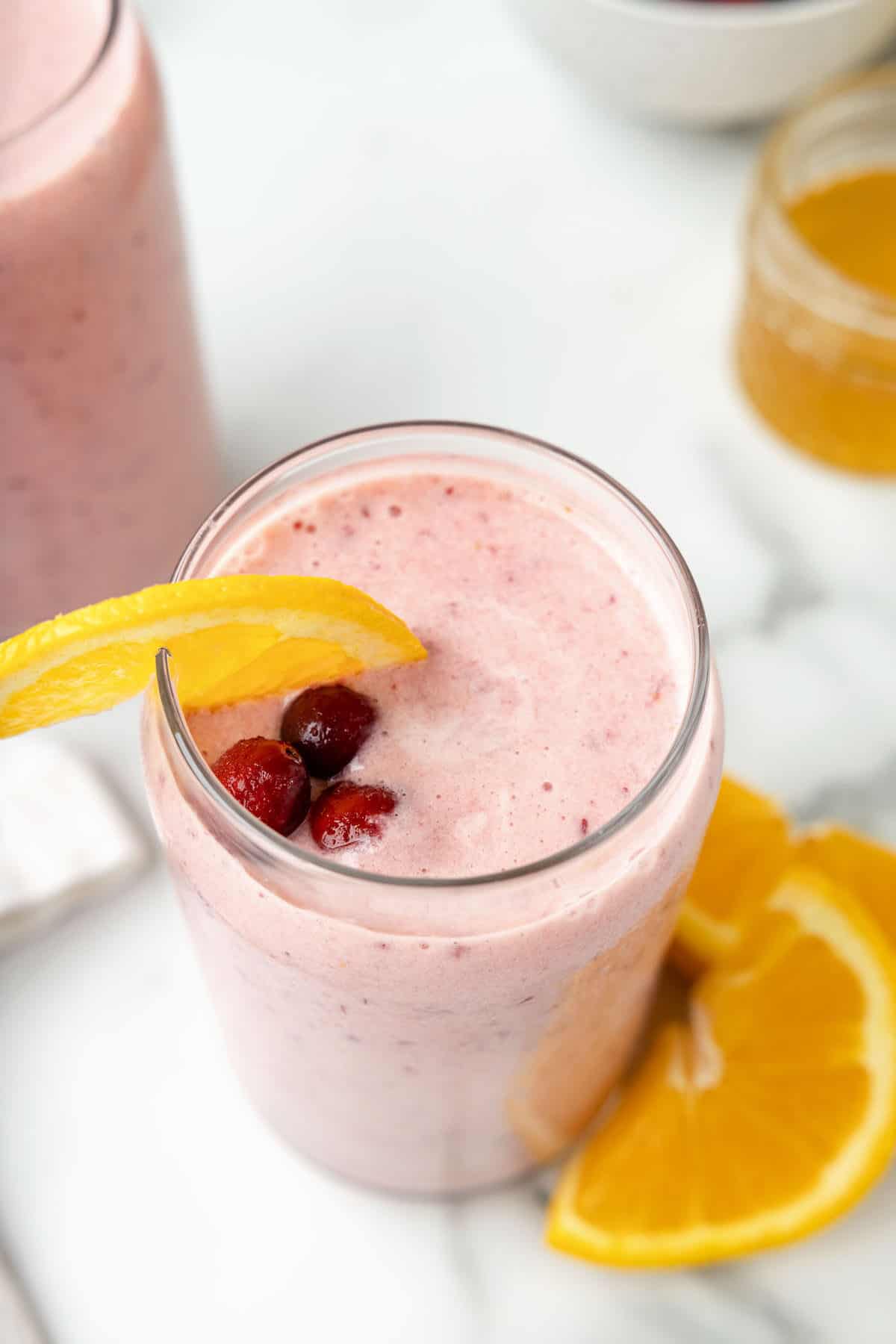 frozen cranberries, wedges of oranges on top of a glass of cranberry smoothie.