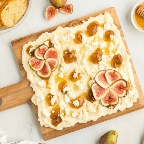 wooden board with butter spread, goat cheese, figs, and fig spread.