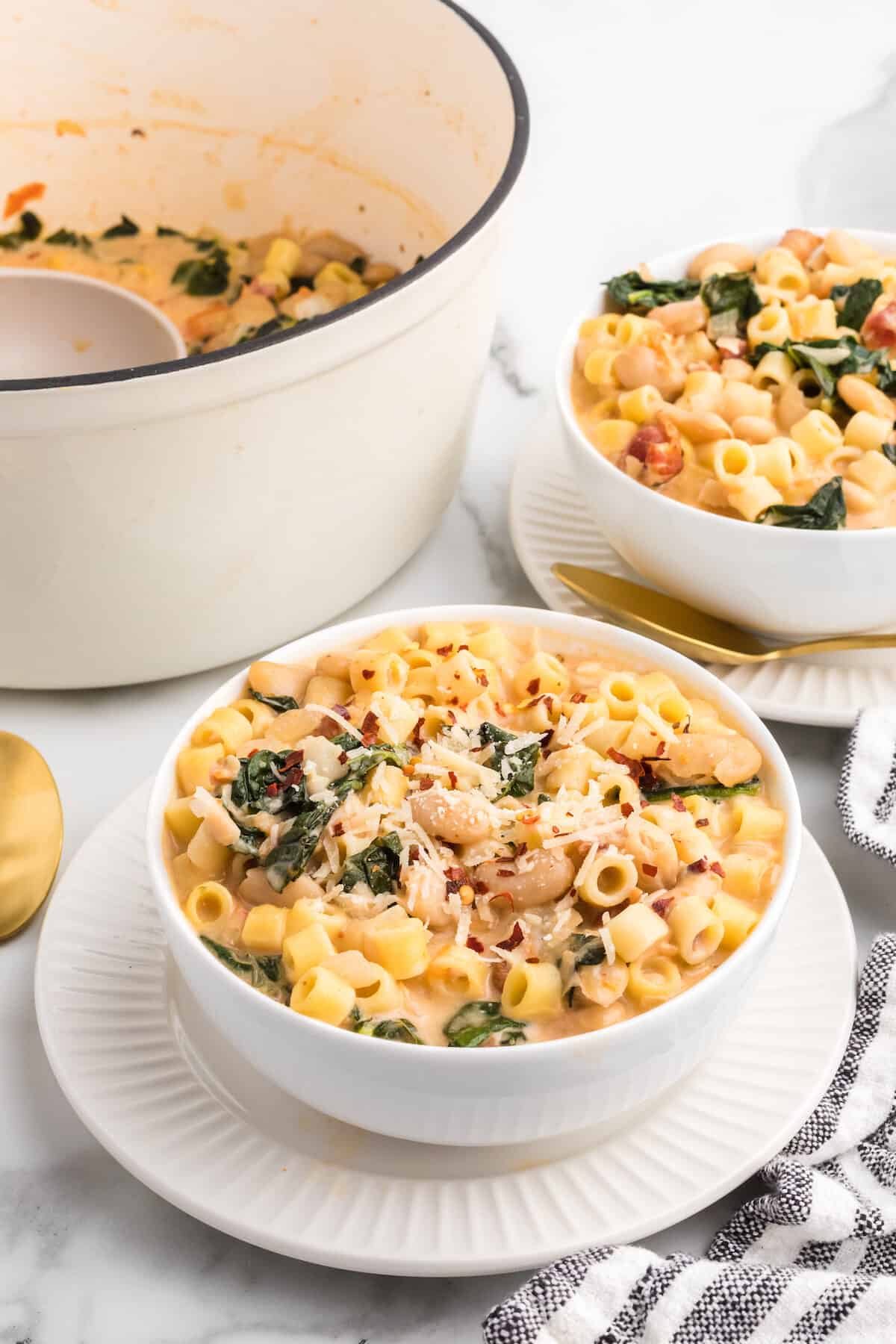 two white bowls of creamy pasta fagioli soup with gold spoons to the side.