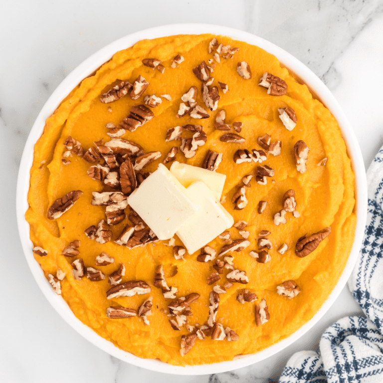 large white bowl with healthy mashed sweet potatoes, topped with chopped nuts, slices of butter.