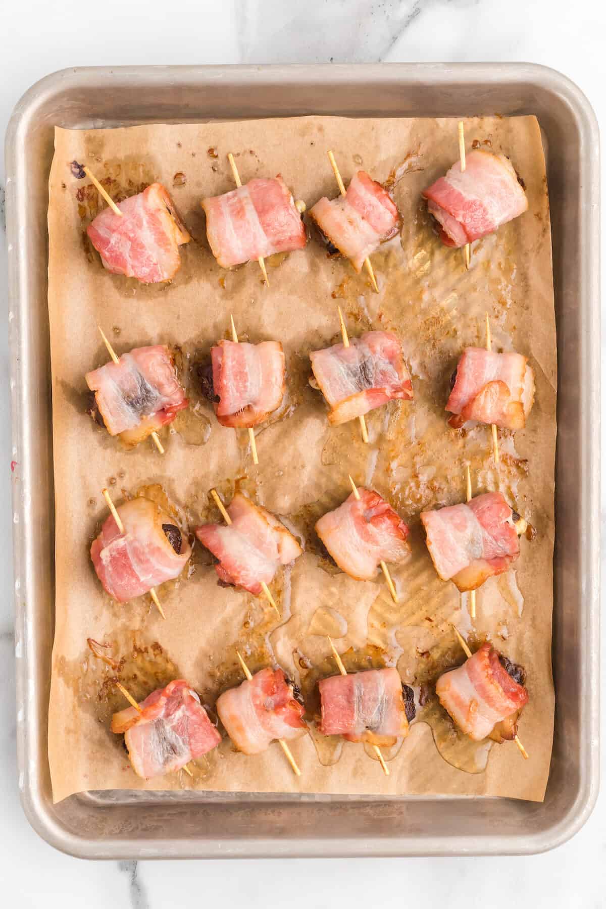 cooked bacon wrapped dates on parchment paper lined baking sheet.