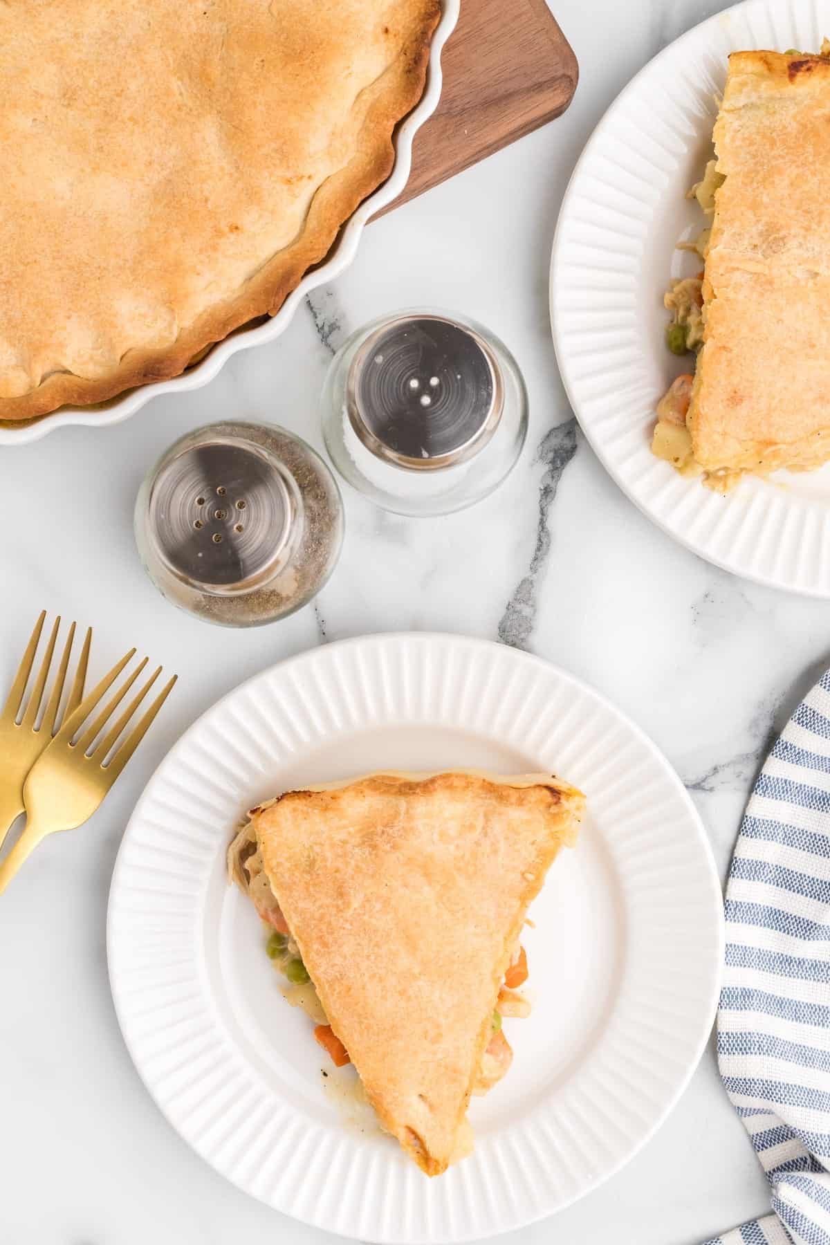 slices of chicken pot pie on white plates with the pie dish in the background.