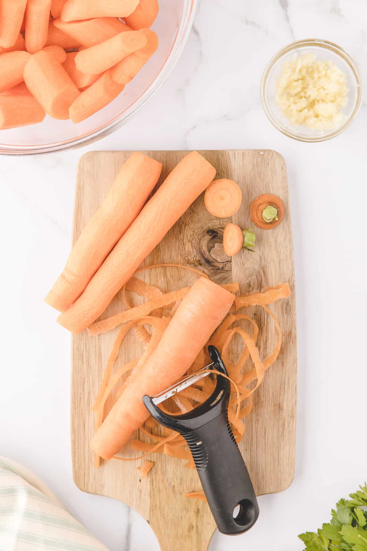 peeling the carrots with a vegetable peeler on a wooden board. 