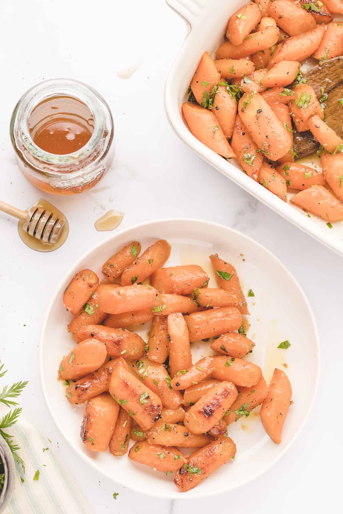 roasted honey garlic butter carrots in a white roasting pan and white plate.