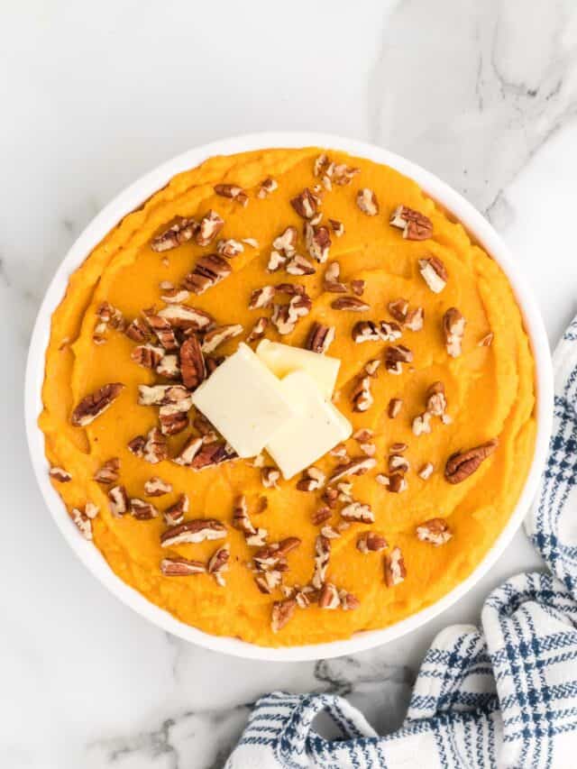 large white serving bowl of mashed sweet potatoes with chopped nuts on top.