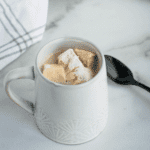 white mug with hot cocoa and healthy marshmallows on top with a black spoon to the side.