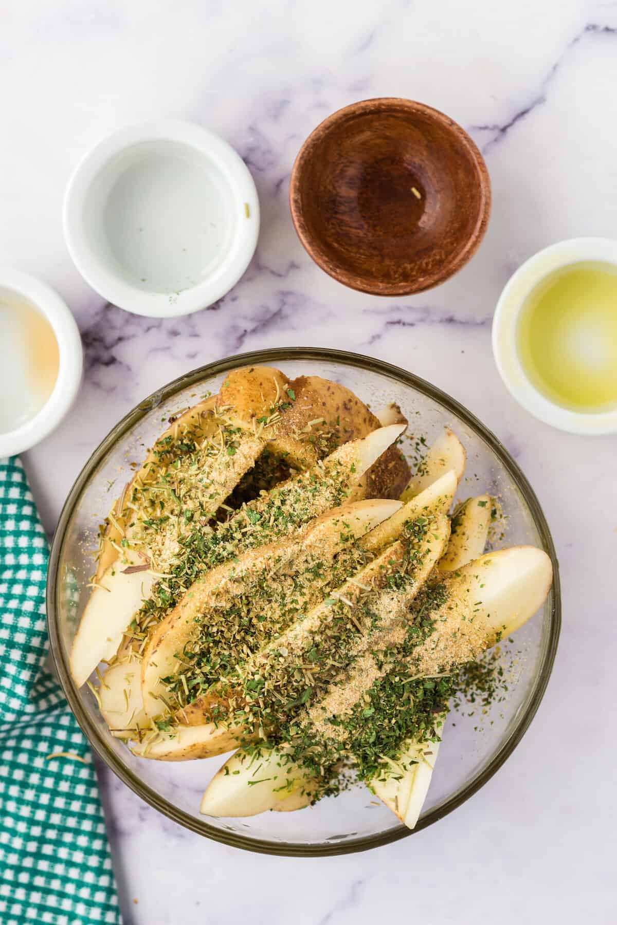 herbs and seasonings on the potato wedges in a glass bowl.