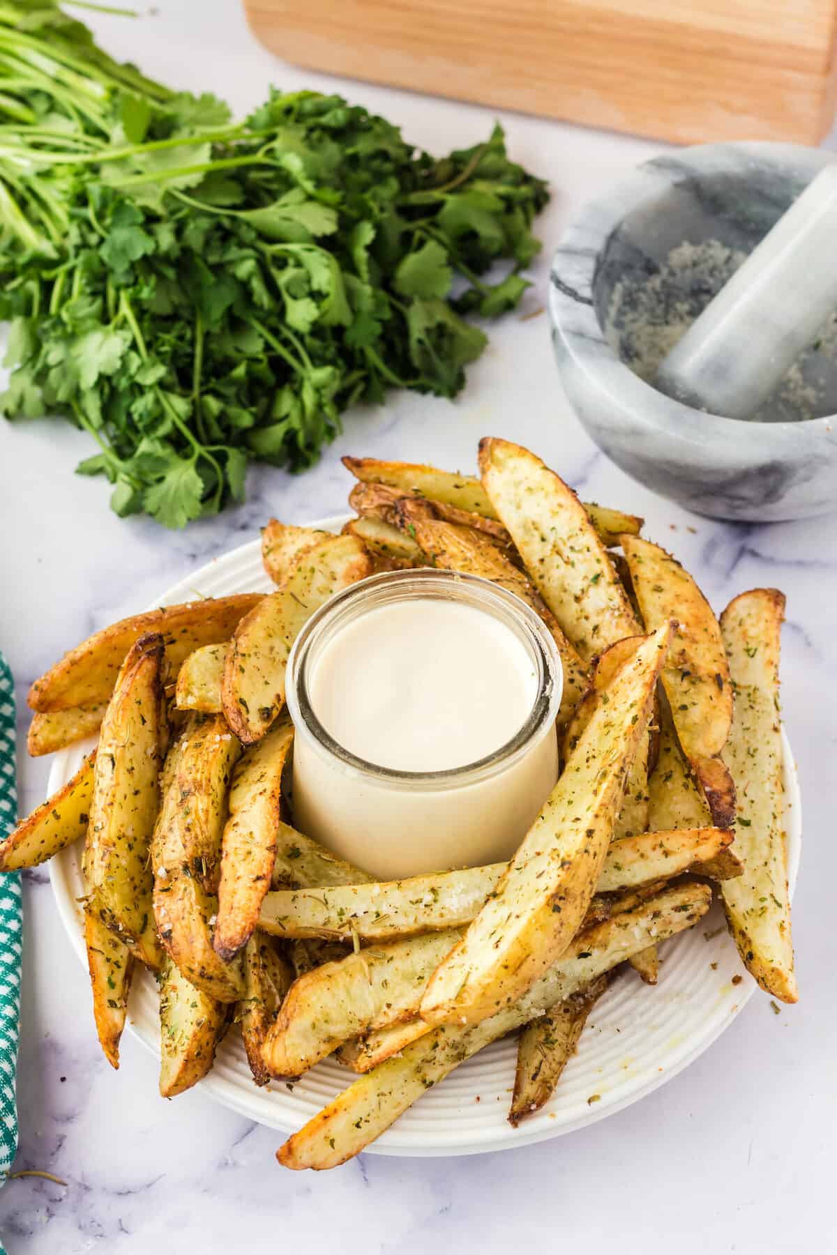 garlic & herb potato wedges with aioli dipping sauce in small jar in center of white plate. 