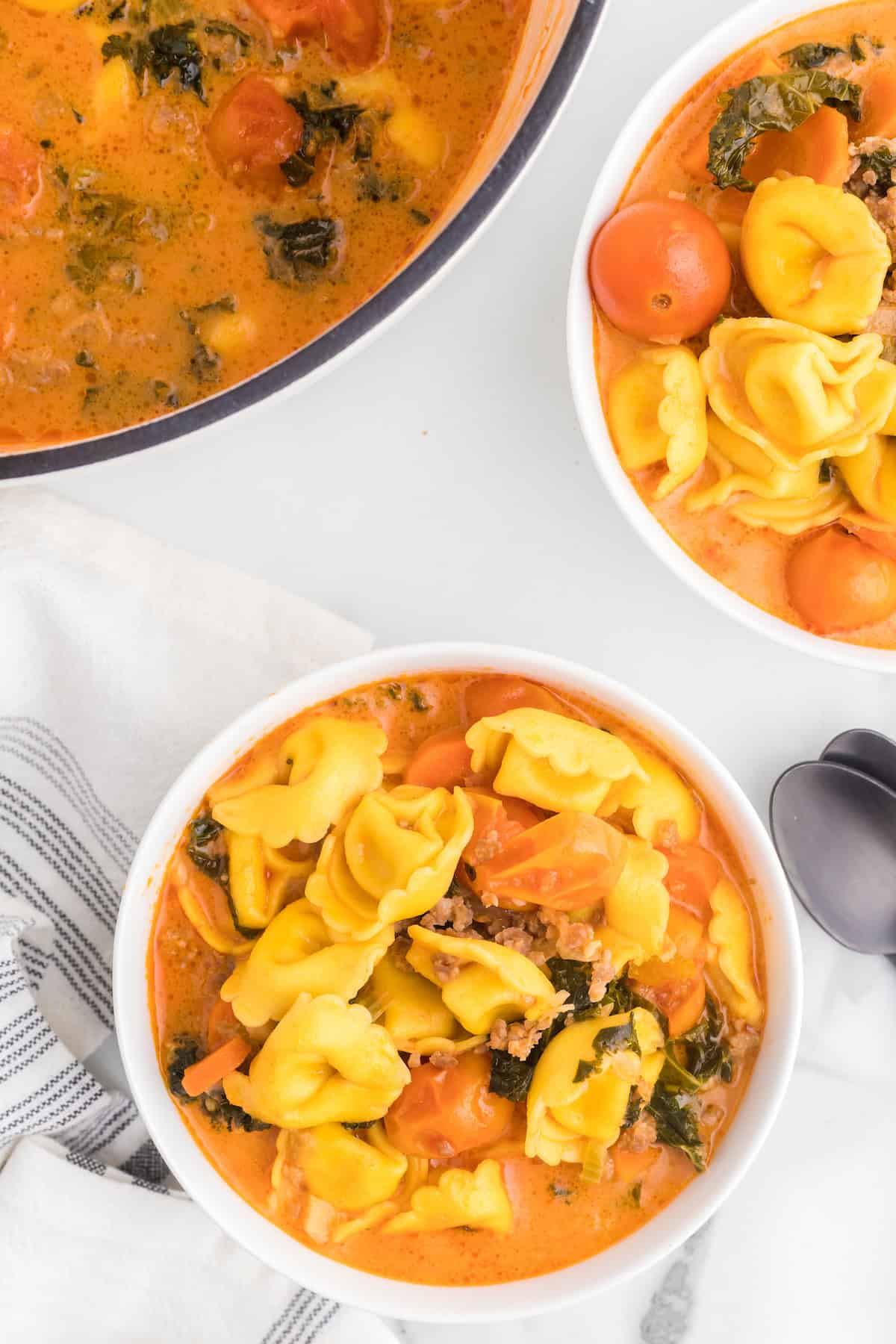 two white bowls filled with creamy tortellini soup with Italian sausage. 