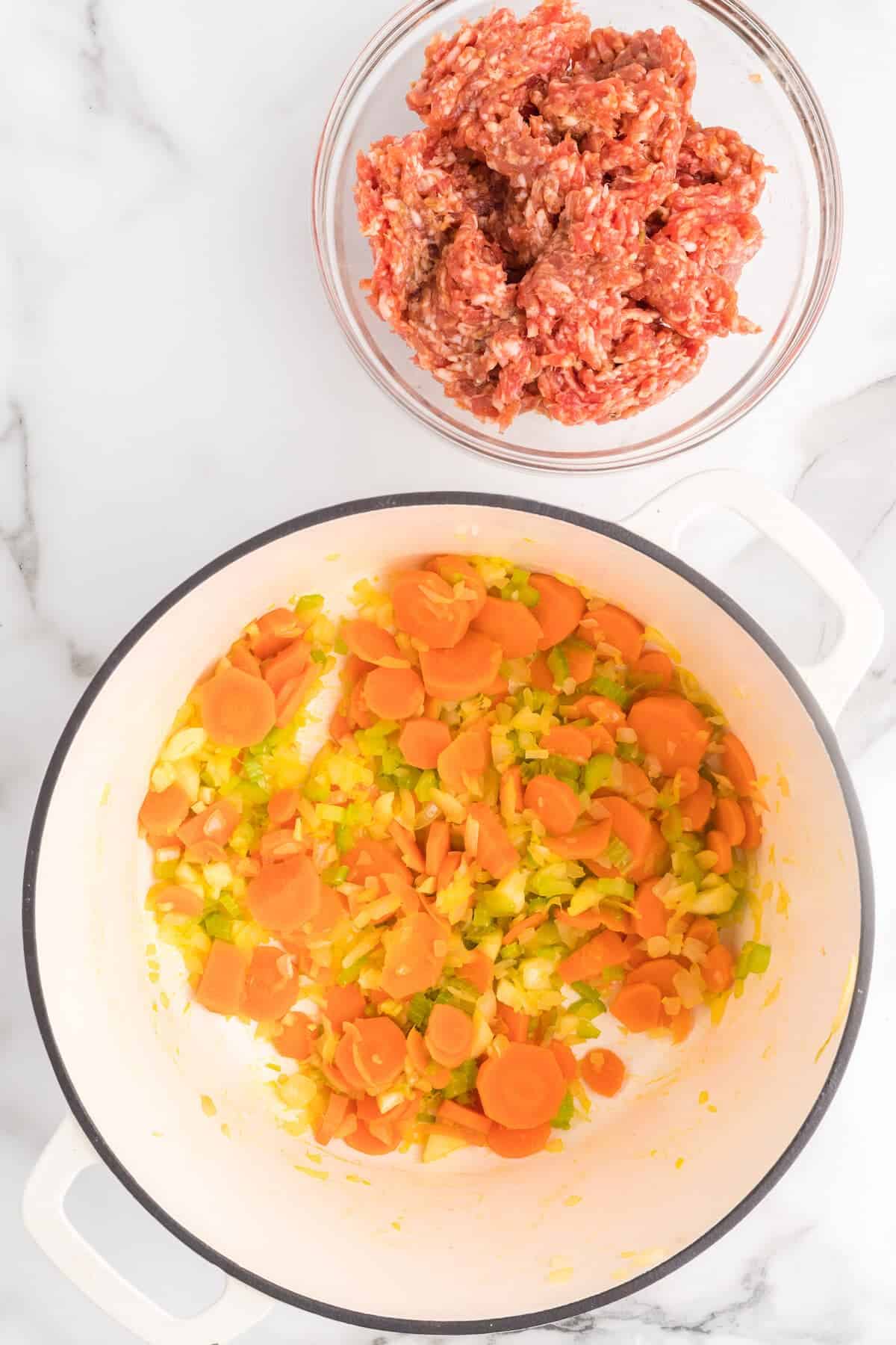 white dutch oven with carrots, onions, and celery.