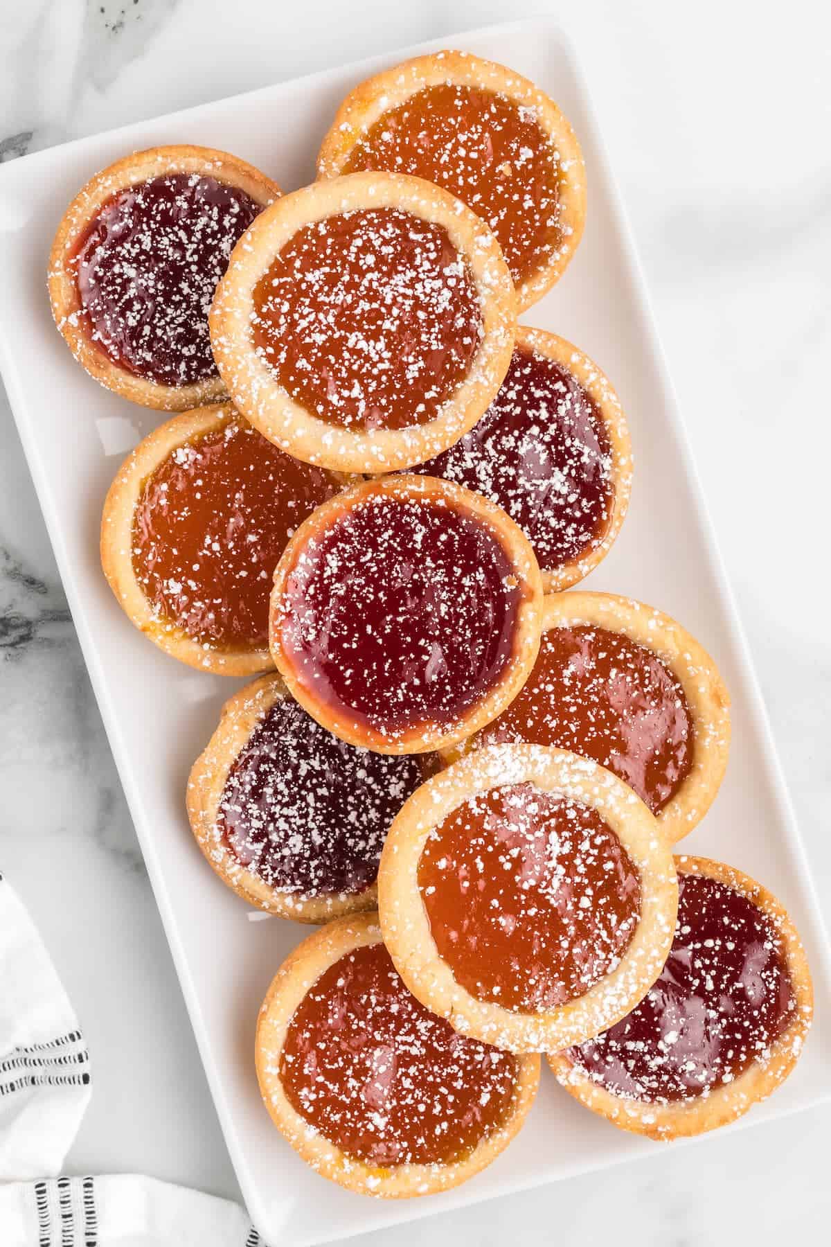 variety of mini jam tarts on a white serving platter.