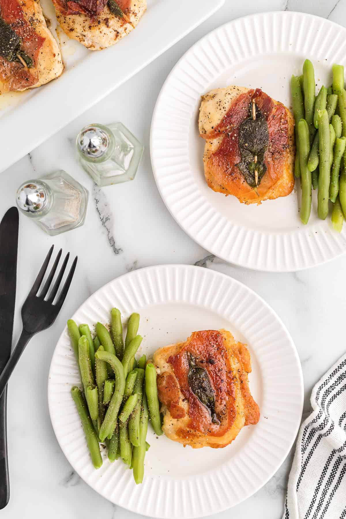 two white dinner plates with chicken saltimbocca and green beans.