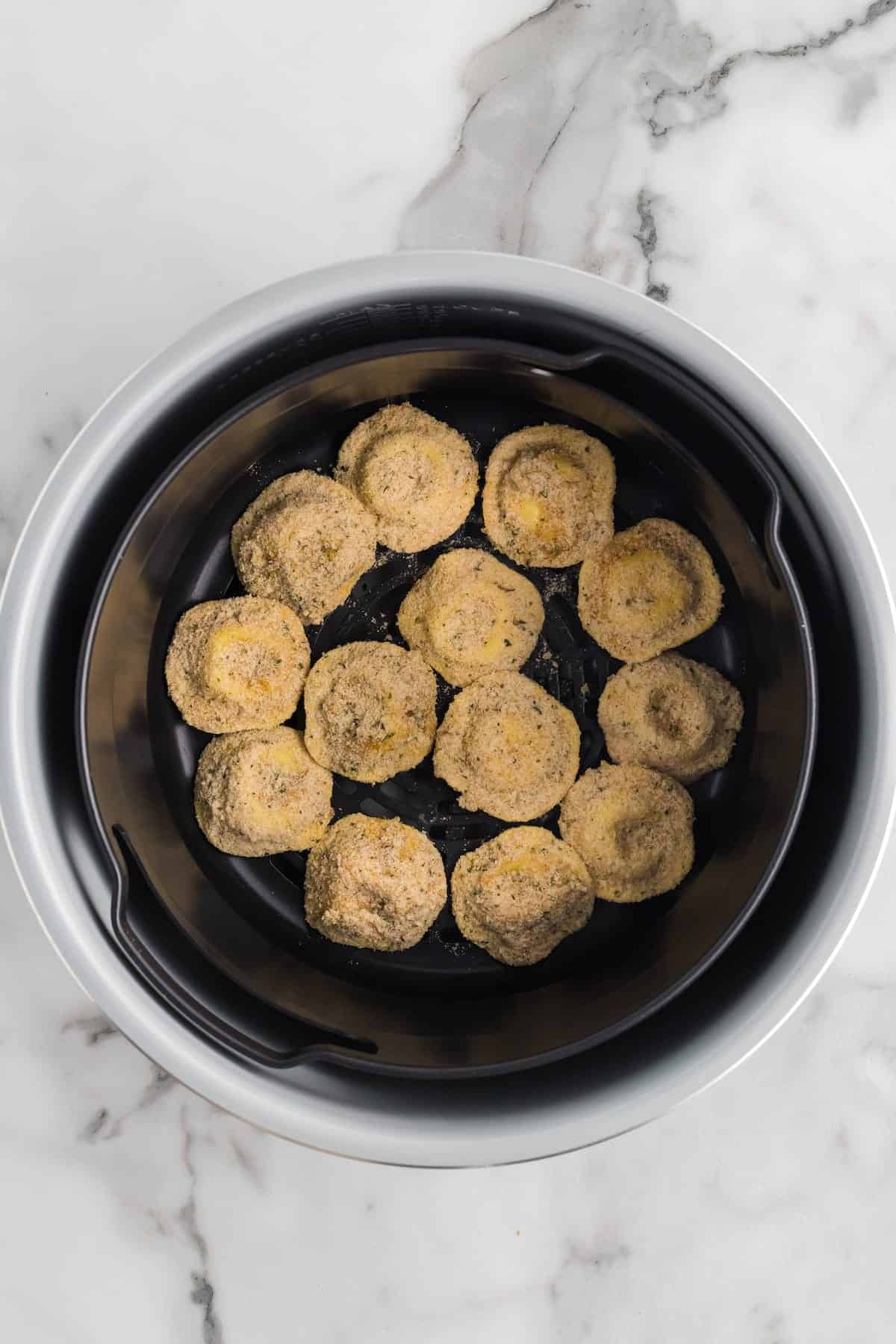 coated ravioli in the air fryer basket.
