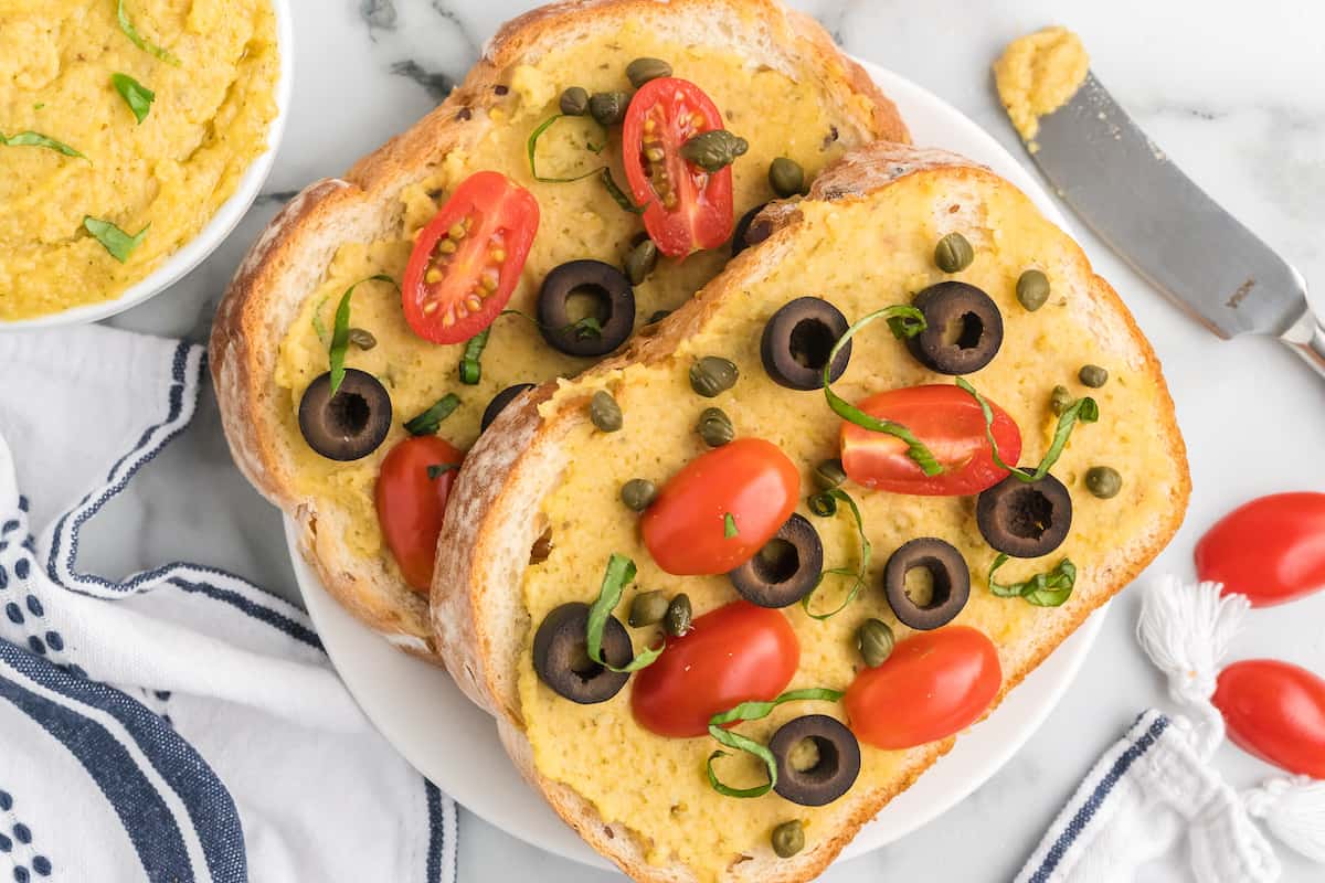 two pieces of toast with homemade hummus and topped with fresh mini tomatoes, capers, and black olives.