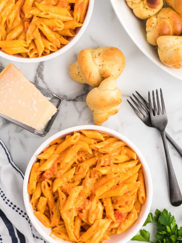creamy pomodoro pasta sauce over penne in white serving bowls. with black forks to the side.