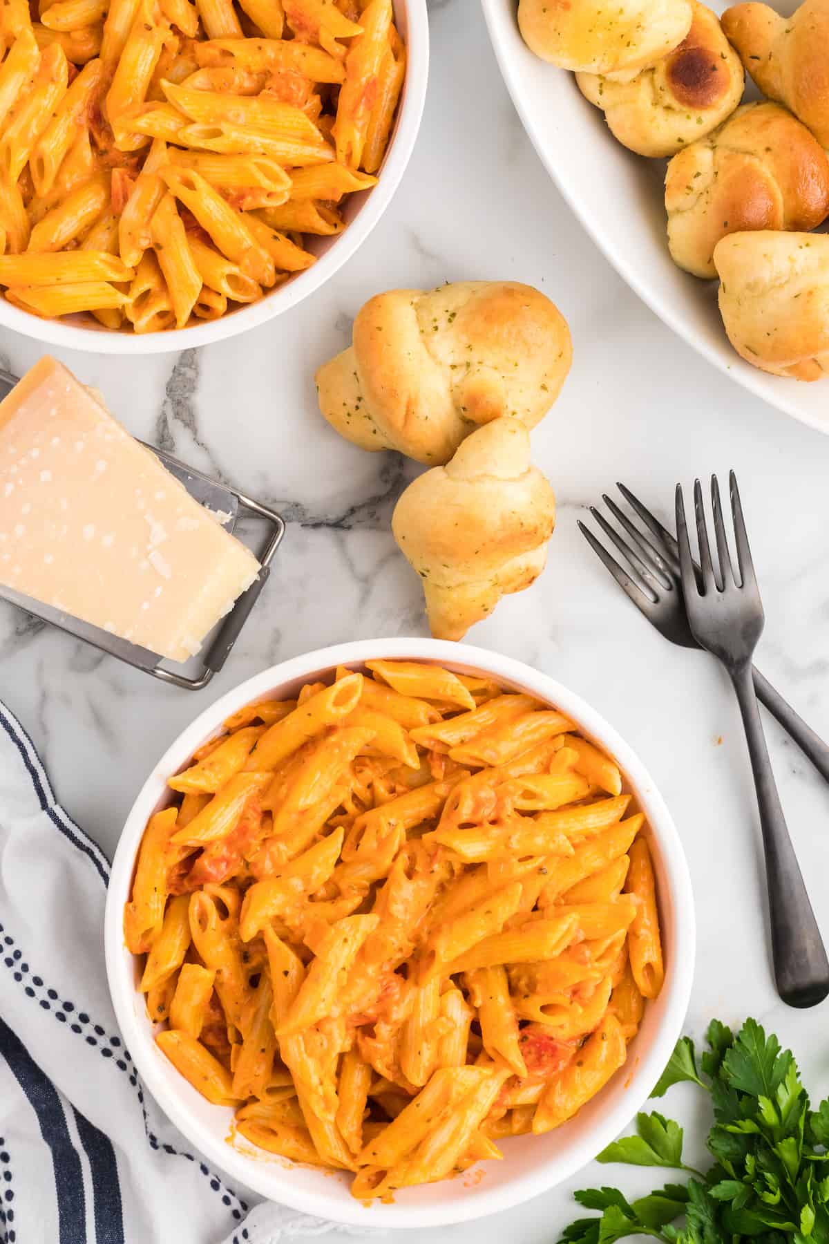 creamy pomodoro pasta sauce over penne in white serving bowls. with black forks to the side.