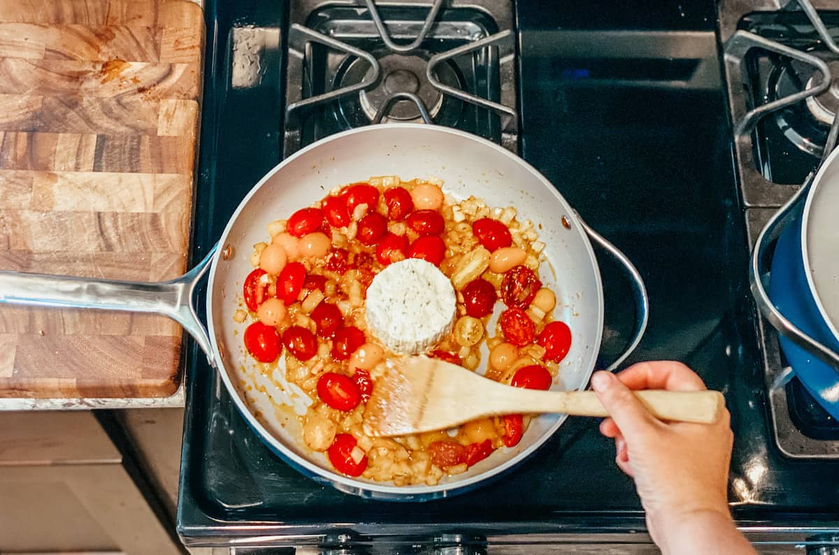 stirring tomatoes with a wooden spoon in the caraway saute pan.