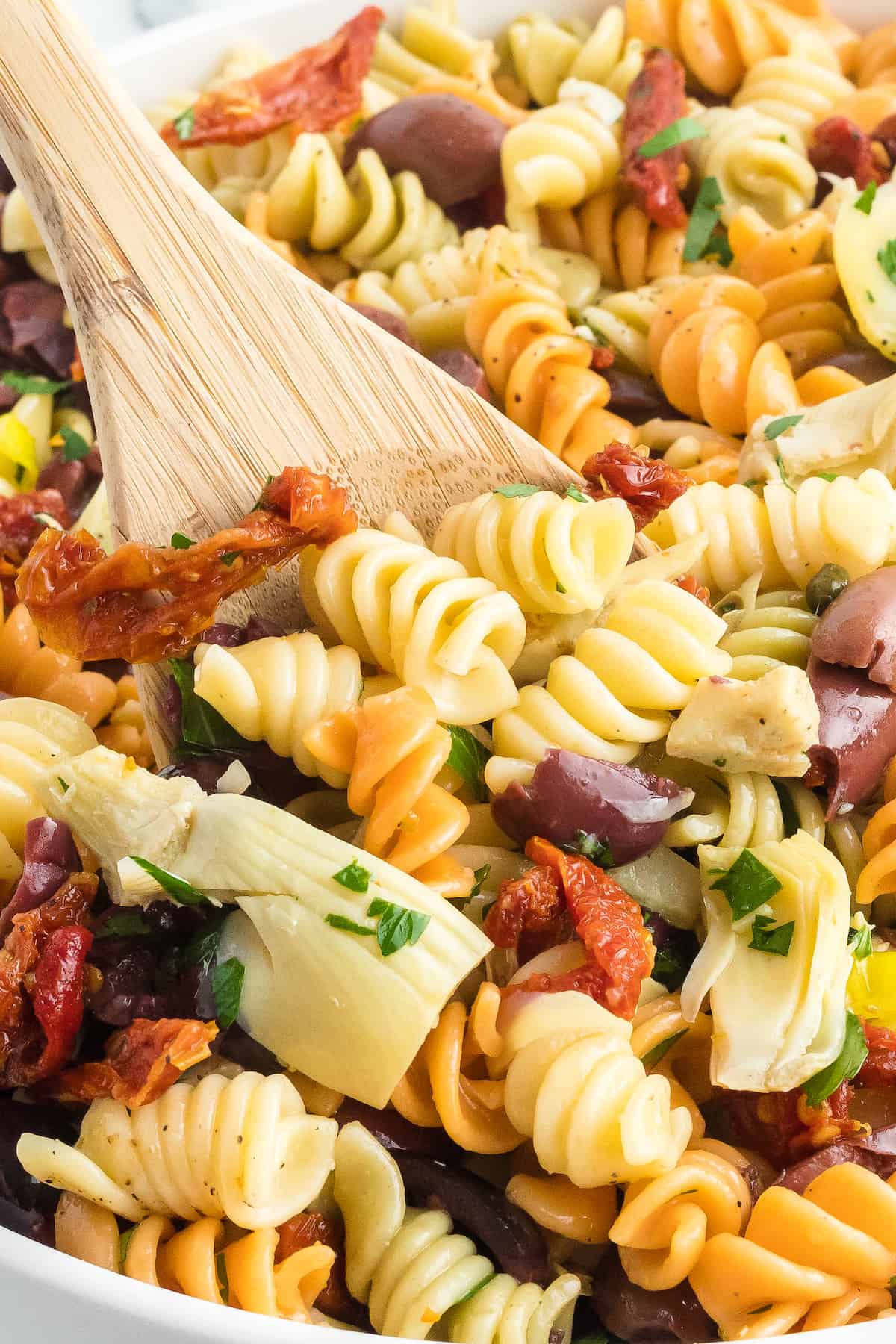 wooden spoon stirring the Mediterranean pasta salad.