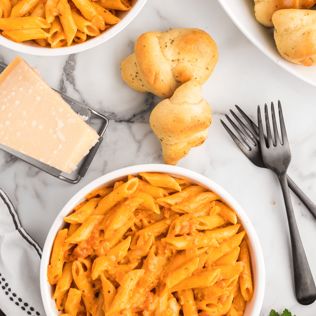 creamy pomodoro pasta sauce over penne in white serving bowls. with black forks to the side.