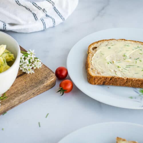 slice of bread with chive butter on top and small white bowl resting to the side.